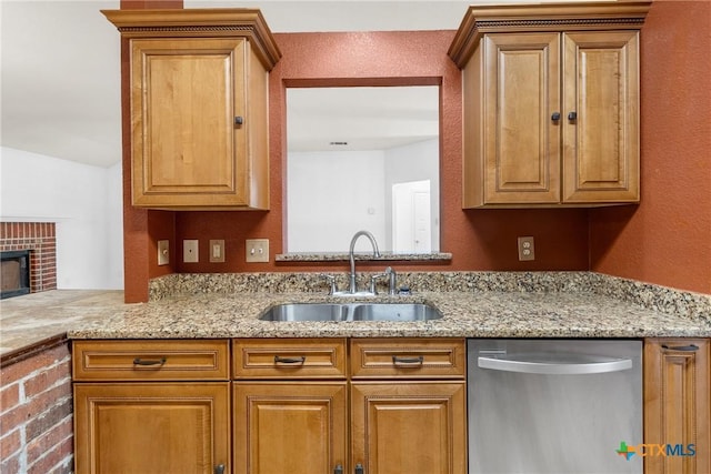 kitchen featuring light stone counters, a fireplace, stainless steel dishwasher, brown cabinetry, and a sink