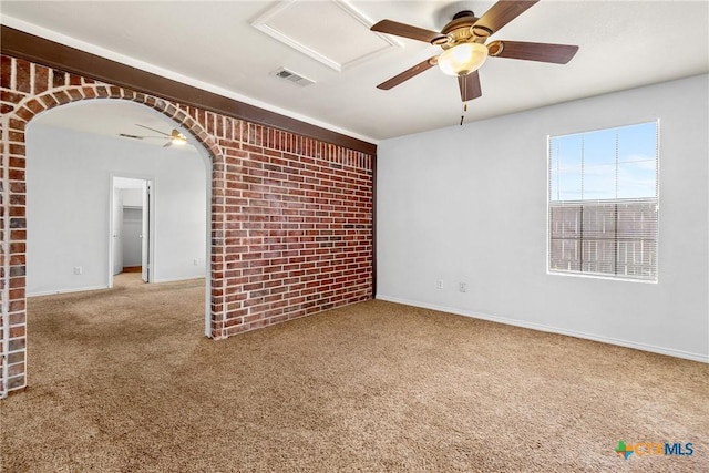 carpeted spare room with visible vents, brick wall, baseboards, arched walkways, and a ceiling fan