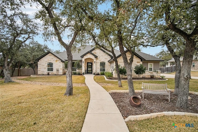 view of front of home featuring a front yard, stone siding, and fence