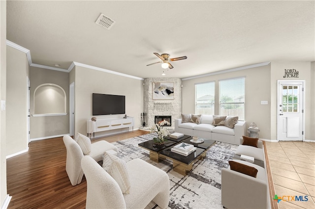 living room featuring a stone fireplace, hardwood / wood-style flooring, ceiling fan, and crown molding