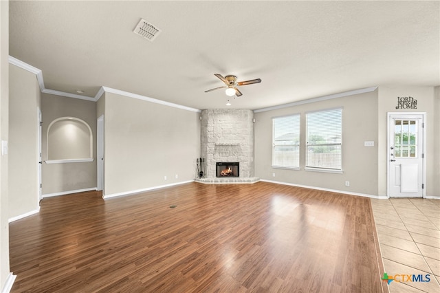 unfurnished living room with ornamental molding, ceiling fan, a textured ceiling, hardwood / wood-style floors, and a stone fireplace