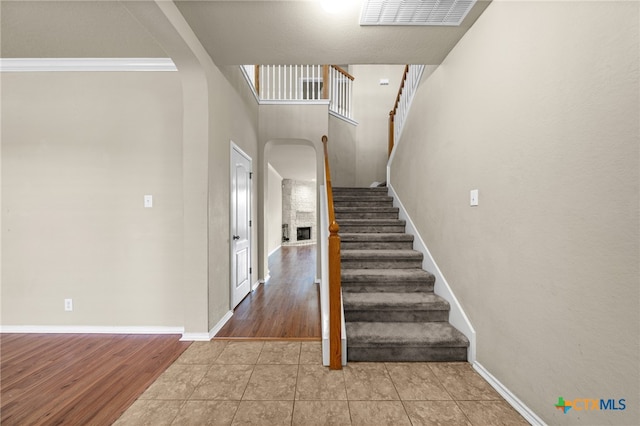 stairs with a towering ceiling, hardwood / wood-style floors, a fireplace, and crown molding