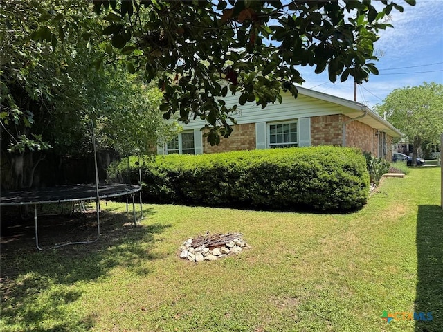 305 Ivy Ave, Luling, TX 78648 - view of side of home featuring a trampoline, brick siding, a yard, and a fire pit