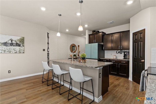 kitchen with a kitchen bar, light hardwood / wood-style floors, a center island with sink, decorative light fixtures, and stainless steel fridge