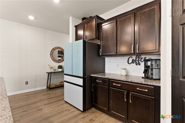 kitchen featuring tasteful backsplash, light stone countertops, dark brown cabinets, fridge, and light wood-type flooring