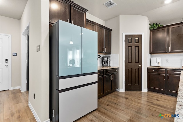 kitchen with dark brown cabinetry, light stone counters, tasteful backsplash, light hardwood / wood-style flooring, and white refrigerator