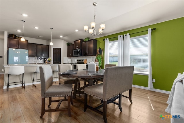 dining space featuring light hardwood / wood-style floors, lofted ceiling, sink, and a notable chandelier