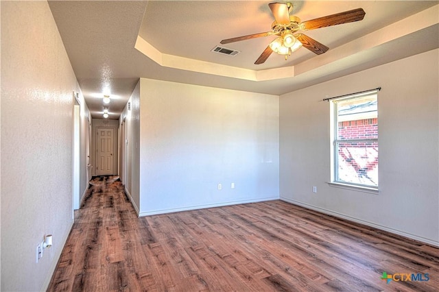 unfurnished room featuring a ceiling fan, visible vents, a tray ceiling, and wood finished floors