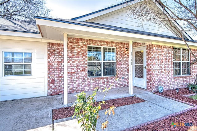 doorway to property with a porch and brick siding