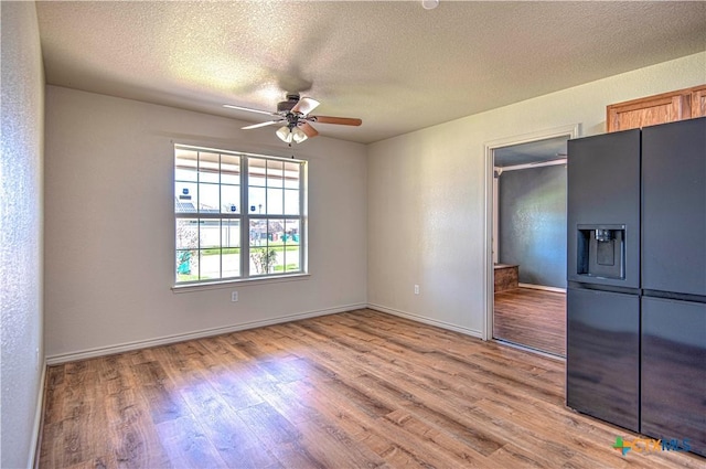 unfurnished bedroom featuring a textured ceiling, ceiling fan, wood finished floors, black fridge with ice dispenser, and baseboards