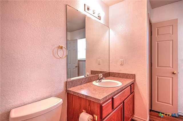 half bath with a textured wall, wood finished floors, vanity, and toilet