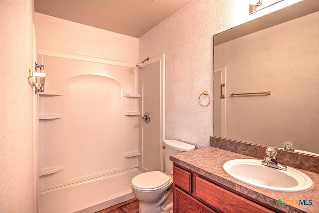 full bath with a shower, a textured wall, vanity, and toilet