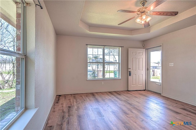 foyer entrance featuring a tray ceiling, ceiling fan, a textured ceiling, wood finished floors, and baseboards