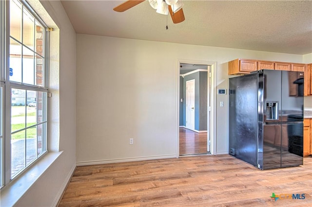 kitchen with light wood finished floors, light brown cabinets, a textured ceiling, baseboards, and black fridge