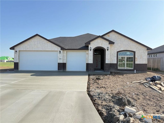 view of front of property featuring driveway, stone siding, fence, an attached garage, and brick siding