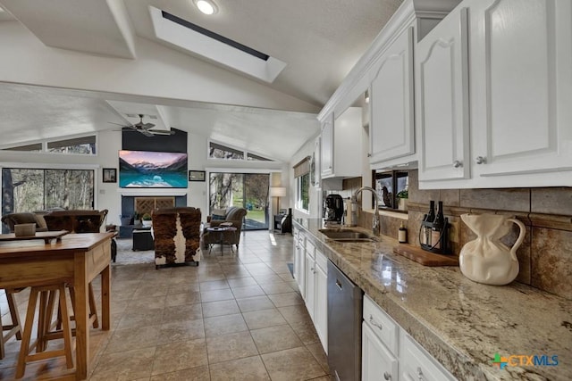 kitchen with vaulted ceiling with skylight, a sink, white cabinets, dishwasher, and open floor plan