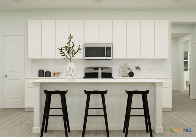 kitchen with a kitchen island with sink, white cabinets, range, and decorative backsplash