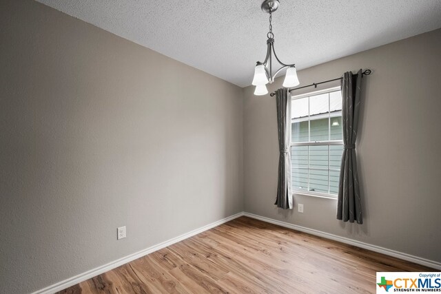 unfurnished room featuring light wood-type flooring, a textured ceiling, and a notable chandelier