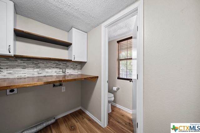 interior space featuring white cabinetry, tasteful backsplash, wooden counters, a textured ceiling, and light wood-type flooring