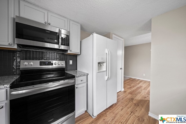 kitchen with appliances with stainless steel finishes, light stone countertops, decorative backsplash, white cabinets, and light hardwood / wood-style flooring