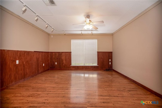 empty room featuring ceiling fan, hardwood / wood-style floors, wood walls, and track lighting