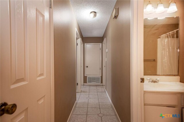 corridor with a textured ceiling, light tile patterned flooring, and sink