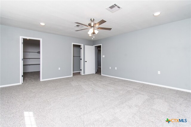 unfurnished bedroom featuring a closet, a walk in closet, carpet, and ceiling fan