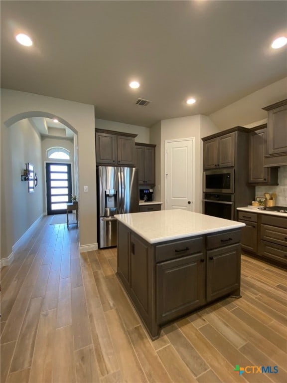 kitchen featuring light wood finished floors, a kitchen island, arched walkways, light countertops, and appliances with stainless steel finishes