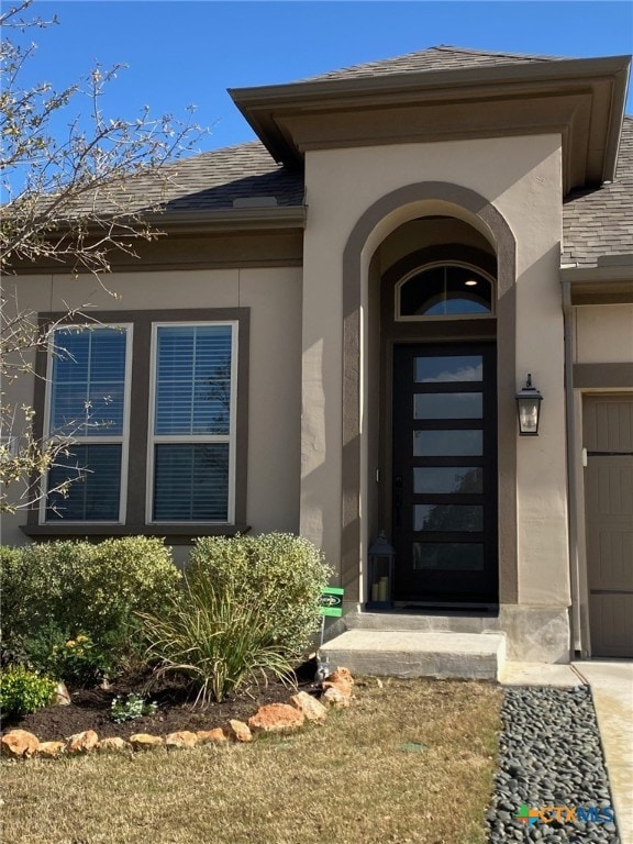 doorway to property featuring stucco siding, an attached garage, and a shingled roof