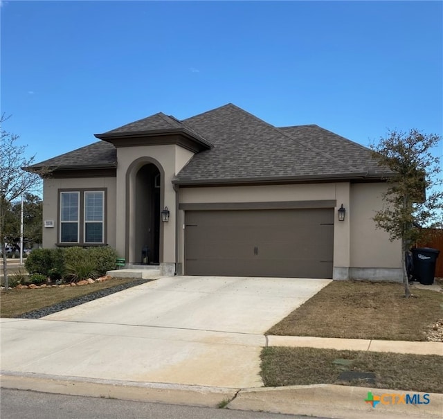 view of front of home with stucco siding, driveway, roof with shingles, and an attached garage