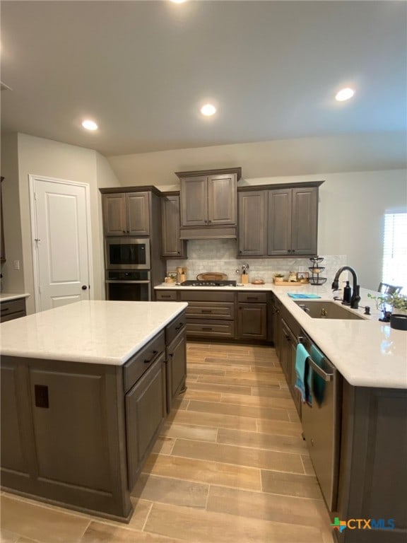 kitchen featuring wood finish floors, a sink, tasteful backsplash, stainless steel appliances, and light countertops