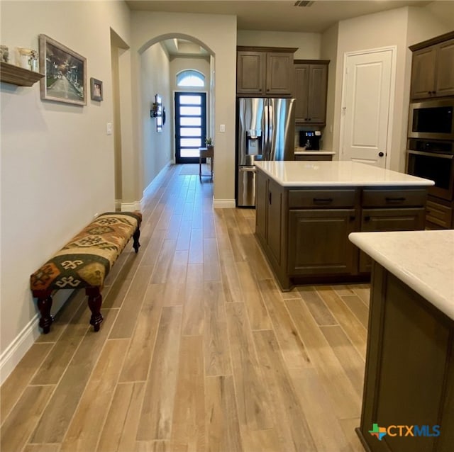 kitchen with arched walkways, appliances with stainless steel finishes, light wood-style flooring, and light countertops