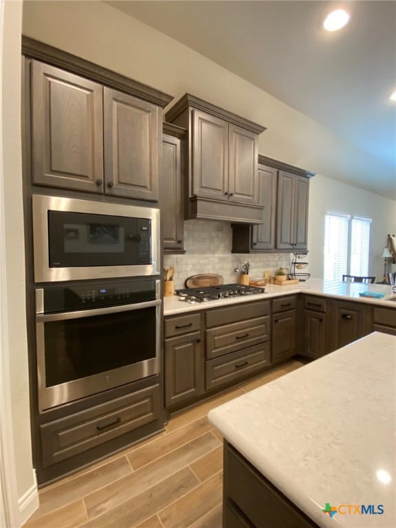 kitchen with wood finish floors, under cabinet range hood, backsplash, appliances with stainless steel finishes, and light countertops