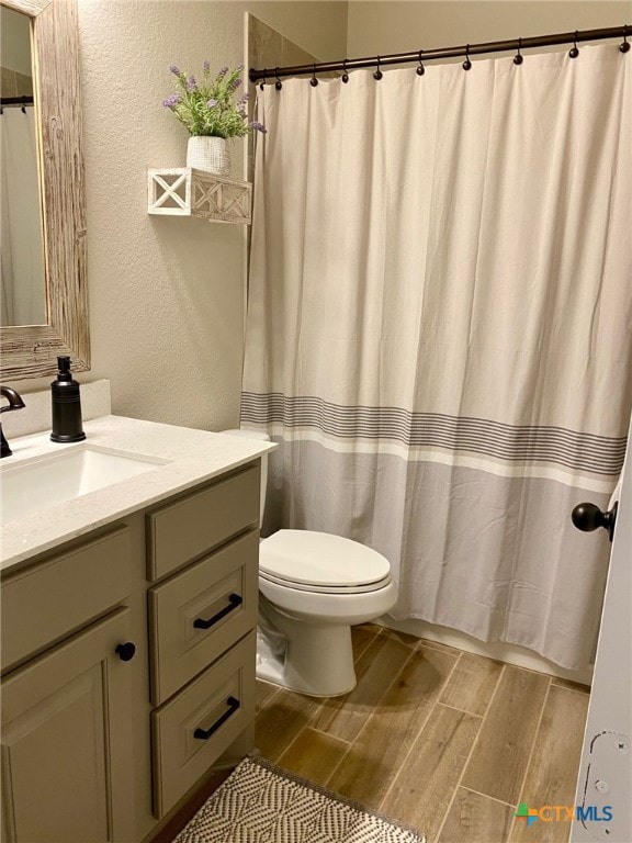 bathroom featuring wood tiled floor, toilet, a shower with curtain, a textured wall, and vanity