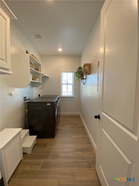 washroom featuring visible vents, washer and clothes dryer, laundry area, baseboards, and wood tiled floor