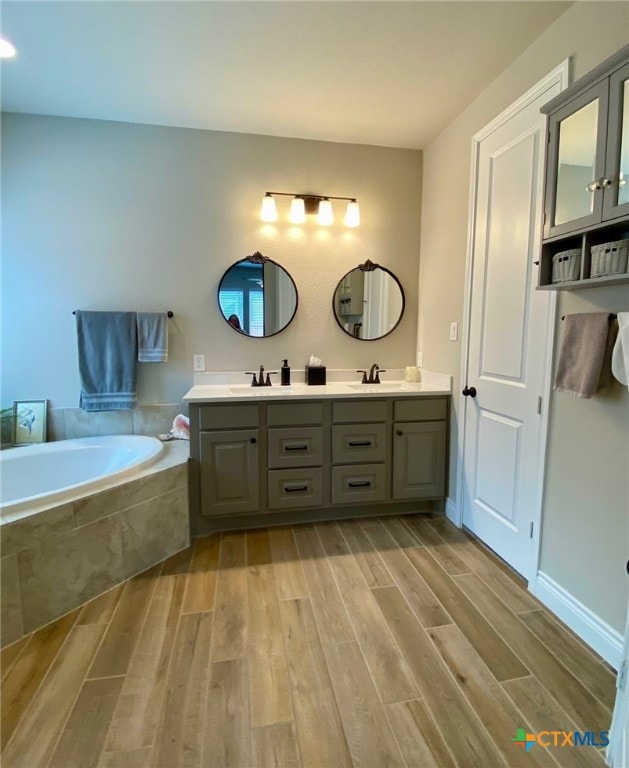 bathroom with a sink, wood finished floors, double vanity, and a bath