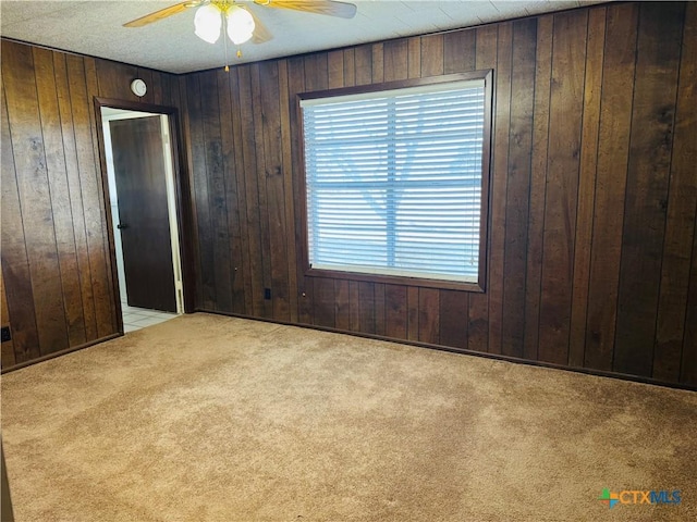 carpeted spare room featuring ceiling fan and wood walls