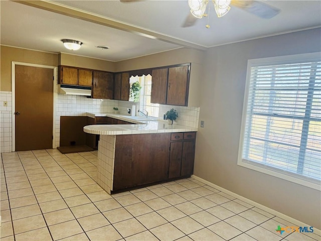 kitchen with decorative backsplash, a wealth of natural light, kitchen peninsula, and light tile patterned floors