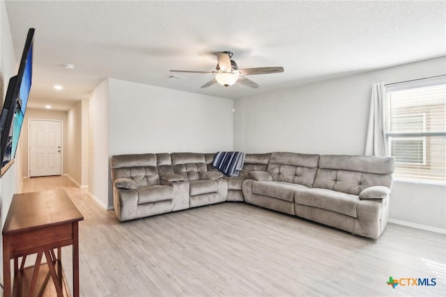 living area with a textured ceiling, light wood-type flooring, a ceiling fan, and baseboards