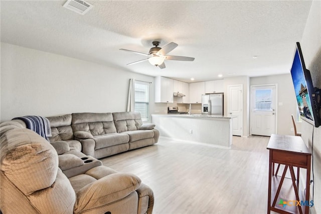 living room featuring a textured ceiling, a ceiling fan, visible vents, and light wood-style floors