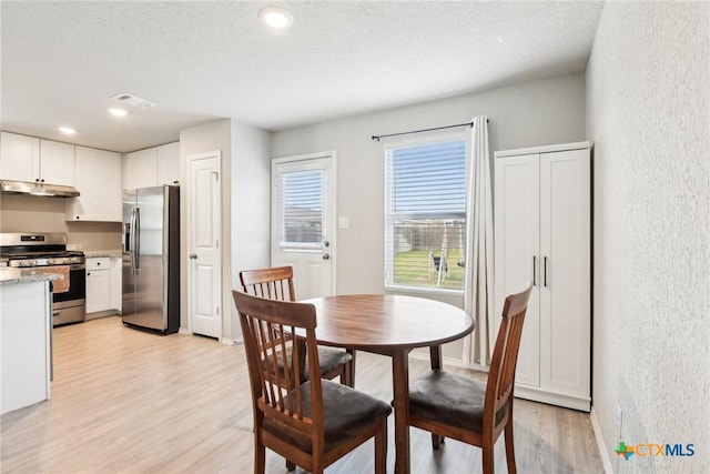 dining space featuring a textured wall, light wood finished floors, visible vents, and baseboards