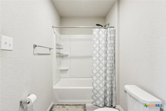 bathroom with shower / tub combo with curtain, a textured wall, and toilet