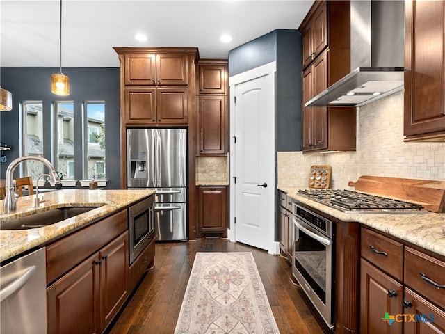 kitchen featuring sink, hanging light fixtures, stainless steel appliances, light stone countertops, and wall chimney exhaust hood