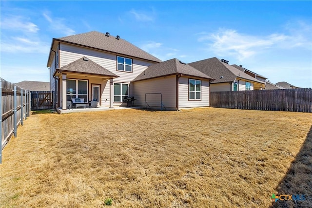 rear view of property featuring a patio area, a lawn, a shingled roof, and a fenced backyard