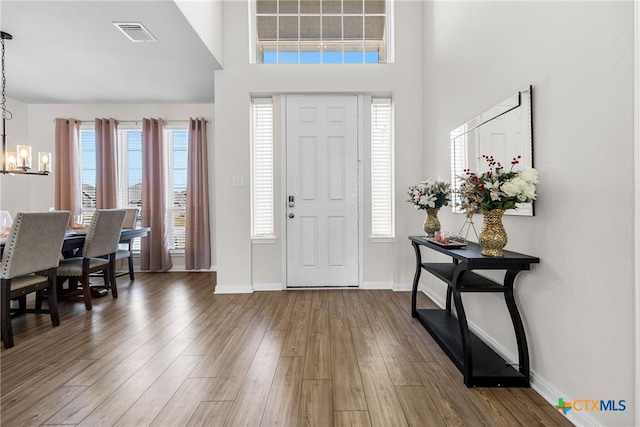 foyer featuring a notable chandelier, wood finished floors, visible vents, and baseboards