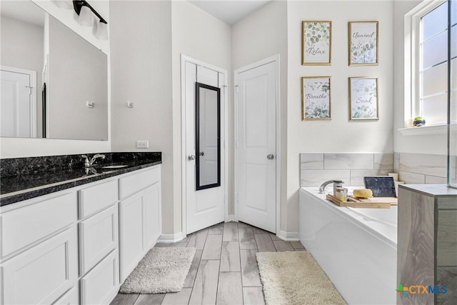 bathroom featuring baseboards, a bath, and vanity