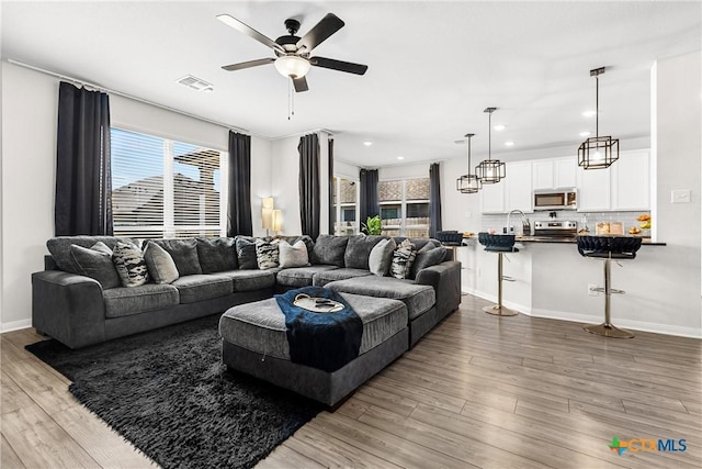 living area featuring a wealth of natural light, visible vents, wood finished floors, and a ceiling fan