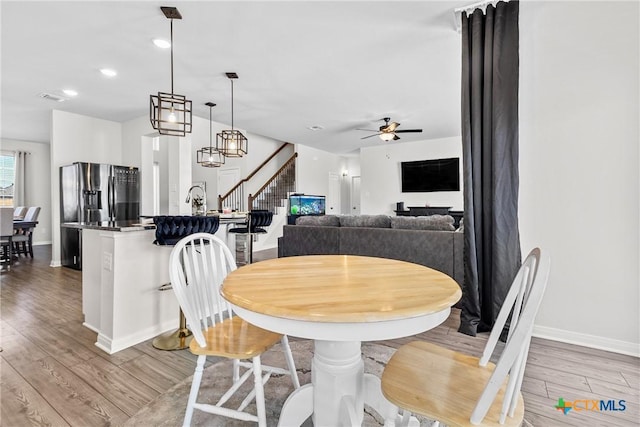 dining room featuring visible vents, a ceiling fan, light wood-style floors, baseboards, and stairs