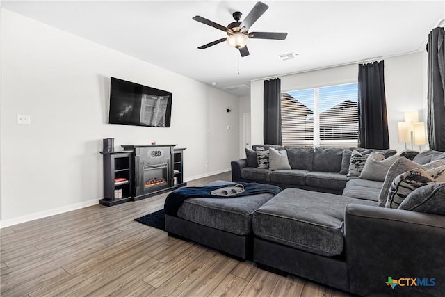 living area featuring light wood finished floors, visible vents, ceiling fan, baseboards, and a lit fireplace