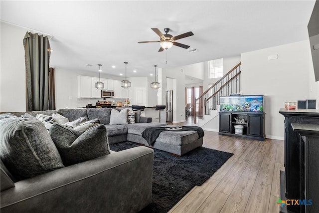 living area with stairway, ceiling fan, baseboards, and light wood-style floors